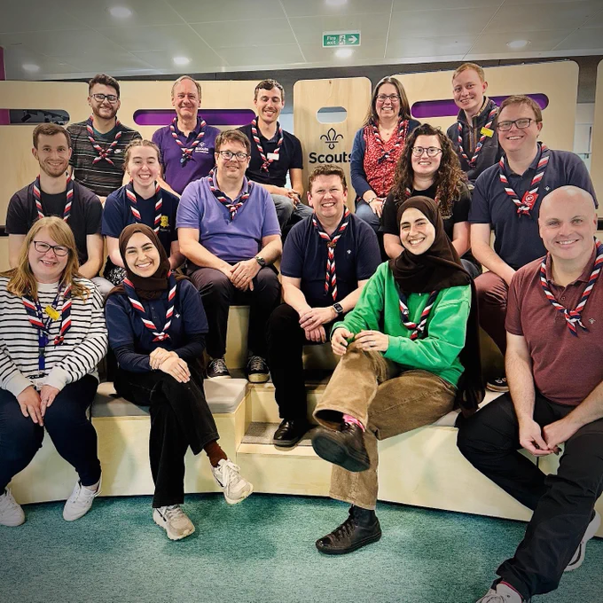 Photo of members of the UK Delegation. There are 15 people in the photo, sitting in an indoor amphitheatre, all smiling and looking at the camera.