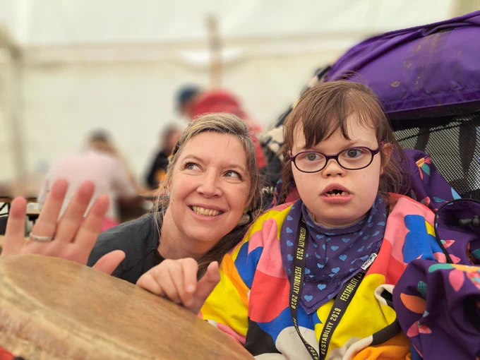 A mum and her disabled daughter play an African drum in a marquee.