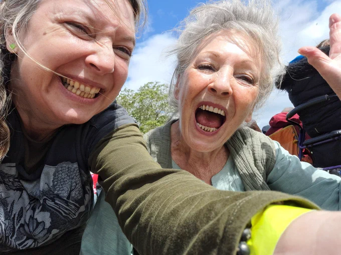 A woman and her elderly mum smile huge smiles into the camera and wave.