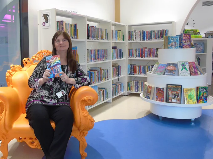 Debbie pictured on the library's orange reading throne at Denny Library holding her winning book.