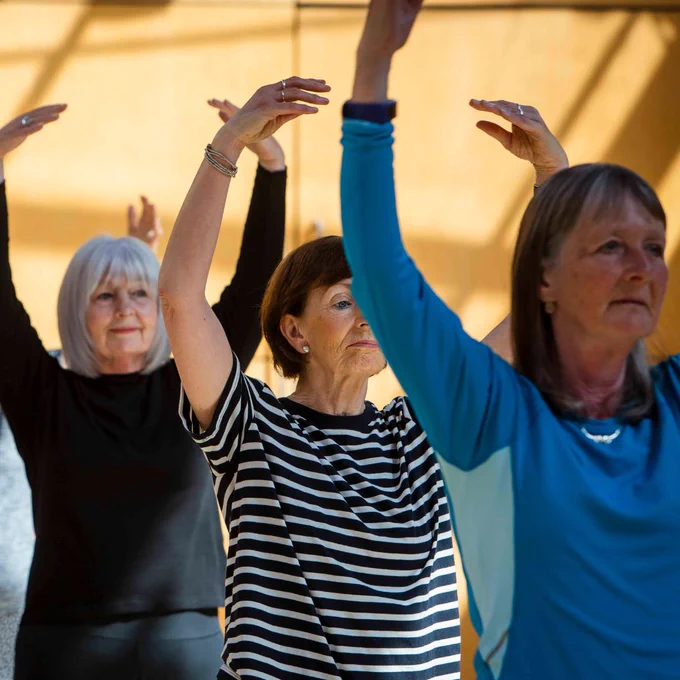 A photograph of a group of three women with their arms raised above their head in a ballet pose. 