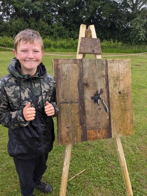 A Scout stands in front on a wooden target with a throwing tomahawk angel embedded in the centre 
