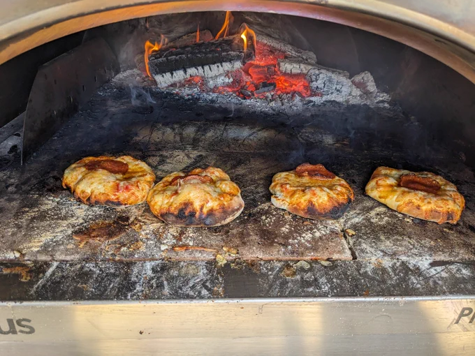 Four small pizzas in a pizza oven with wood embers at the back