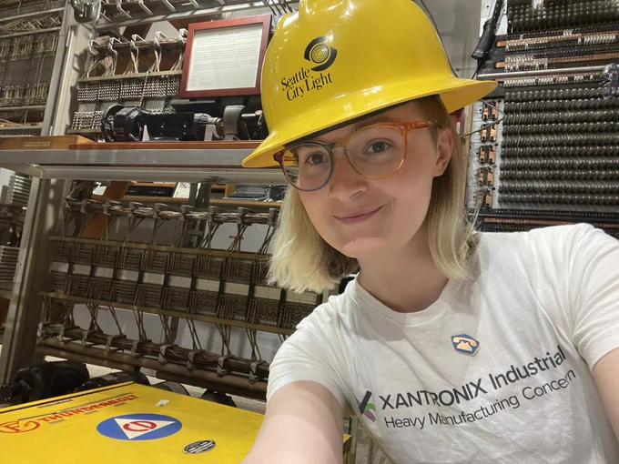 claire and a yellow thunderbolt air raid siren wearing a yellow seattle city light hard hat