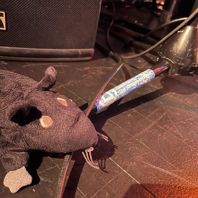 Zeke on the edge of the Fitzgerald's stage, St Paul, with his mouth on an equipment wire. There's a nearby sticker on a stand's foot from the old Dial A Song days, illustrating that They Might Be Giants anagrams to Get Atheism By Night