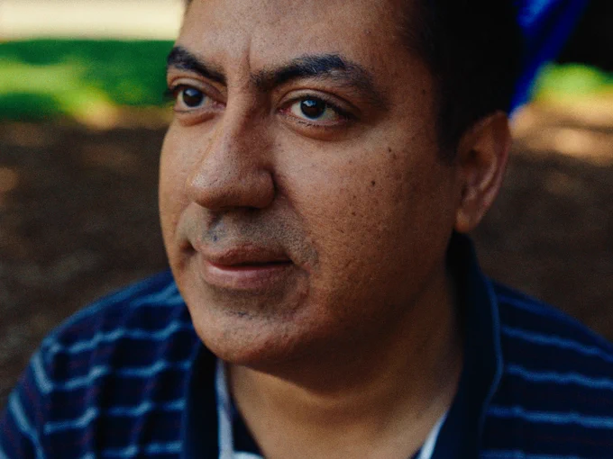 The camera focuses close as a man looks off camera and smiles softly.