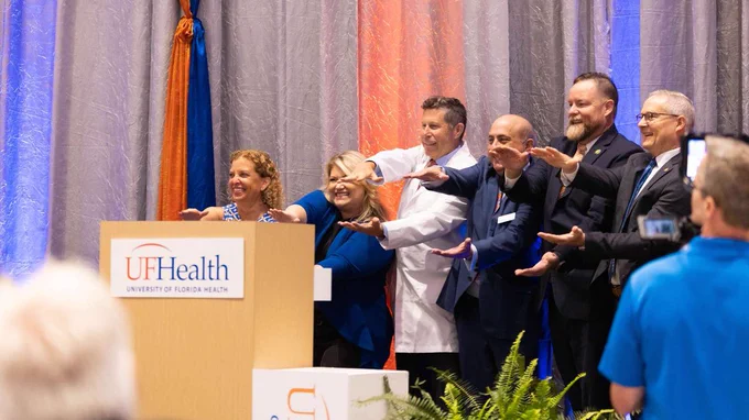 A group of legislators and UF Health officials celebrate with the Gator Chomp during the NCI announcement.