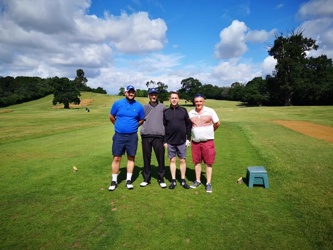 Four men standing in a row on a golf course.