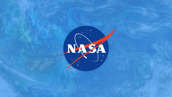 A graphic of the NASA "meatball" insignia against a blue, wavy background resembling an ocean as seen from above. The meatball is a dark blue circle, intersected by a red "V" and spotted with white stars. The text "NASA" appears on the circle in a white serif font, with a stylized white circle symbolizing an orbiting satellite surrounding it. Credit: NASA