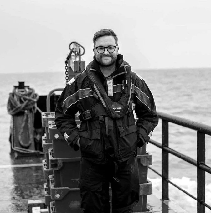Olly Reed on a boat at sea in a black and white photo
