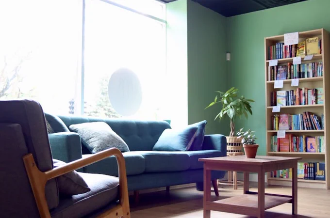 Photo of Call & Response Books’ interior, showing a blue couch, armchair, plants, and wooden bookshelves filled with books.