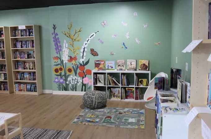 Photo of Call & Response Books’ interior, showing the kid’s corner with picture books, a tall flower mural, and kids’ seating.