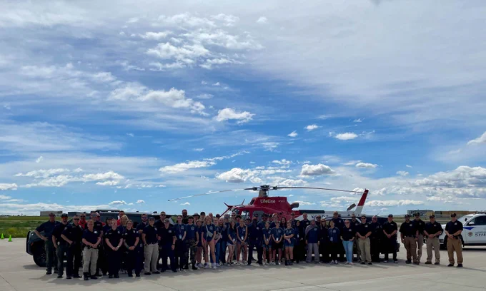 A large group of students and law enforcement partners from Fort Collins Police Services, Larimer County Sheriff's Office, and Timnath Police Department smile for a photo in front of police vehicles and a helicopter at this year's Youth Police Academy.
