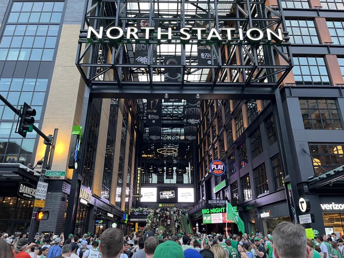 Streams of people, many dressed in green, head in the streetside entrance to North Station in Boston.
