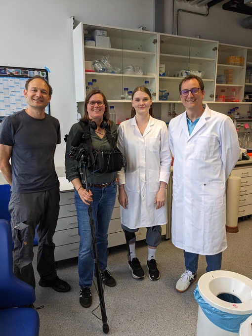 Group photo of four people standing next to each other, two belonging to a film crew that are making a documentary for school children and two scientists wearing lab coats, who were being interviewed by the film crew