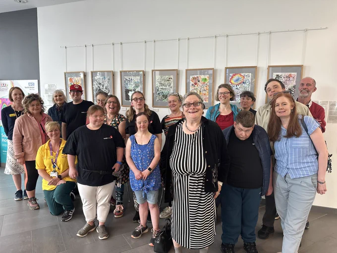 18 people from misfits and creative shift stood together infront of their colourful framed art work all smiling proudly.