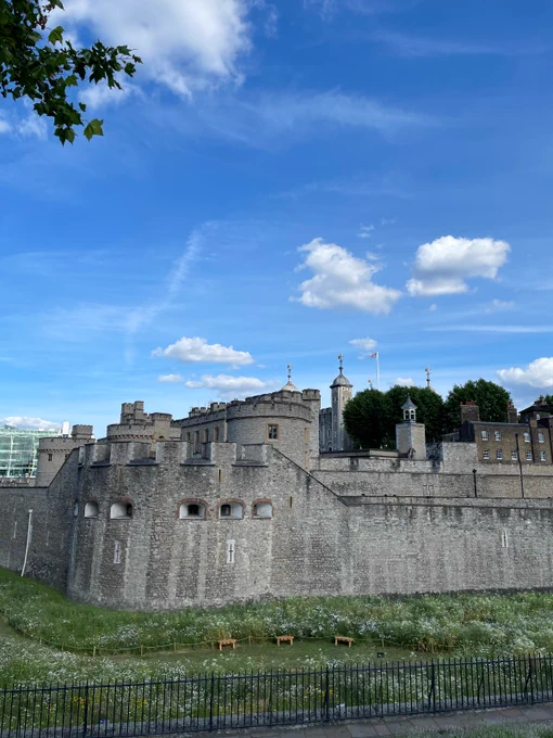 A flower-filled moat in front of the external brick walls of the Tower of London with the White Tower at the centre