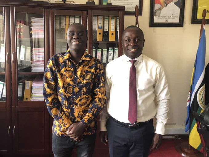 A photo of me on the right and the sports minister on the left in an office background with file board and flags