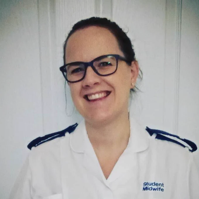 Irwin Mitchell client, Sarah wearing a medical uniform with "Student Midwife" embroidered on it, standing in front of a white door.