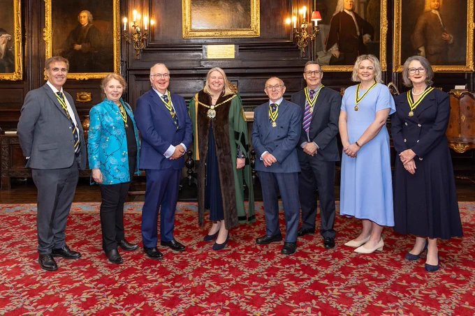 The seven new Liverymen standing with the Master Liz Shilling in the Apothecaries' Court Room. All are smiling broadly and dressed smartly. (C) Mark Witter Photogrpahy.