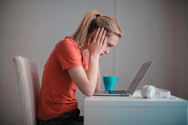 This person is staring at a laptop looking frustrated with head in hands.