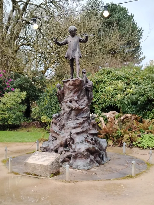 A statue of Peter Pan, playing the pipe, surrounded by fairies, rabbits, and other woodland creatures. 