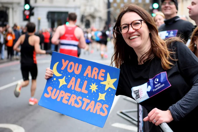 A person cheering on London marathon runners. She is holding up a hand-painted banner that reads 'you are all superstars.'