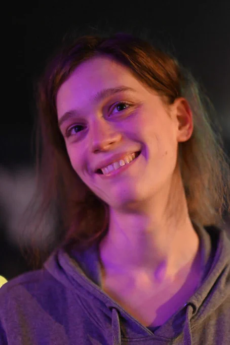 Sophie wearing a hoodie to the local lesbian poetry night. The photo captures her smiling while lit by purple light.

Photo credit Léa Junger
