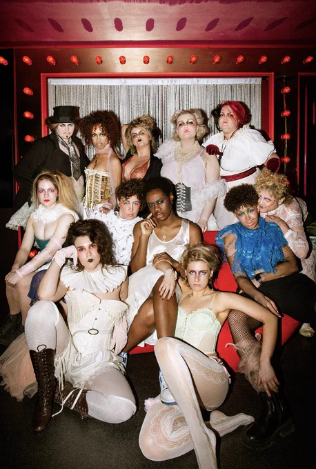 The cast of Taming of the Shrew, in burlesque / cabaret wear, draped together over a large sofa, with red lights behind 