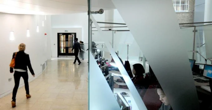 People using the desktop computers in the e-Library space on the ground floor of Keppel Street. Other people can also be seen passing this room on the left hand side.
