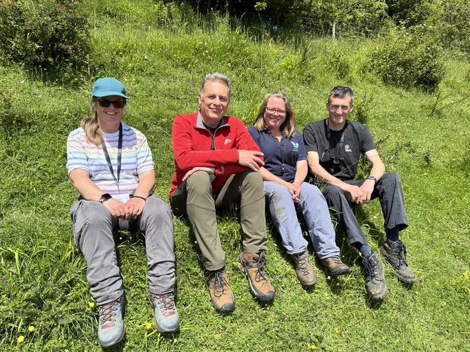 Sarah from the Royal Entomological Society, Chris Packham, Caroline from Butterfly Conservation and Mark from Somerset Wildlife Trust sat together on a grassy bank, smiling at the camera.