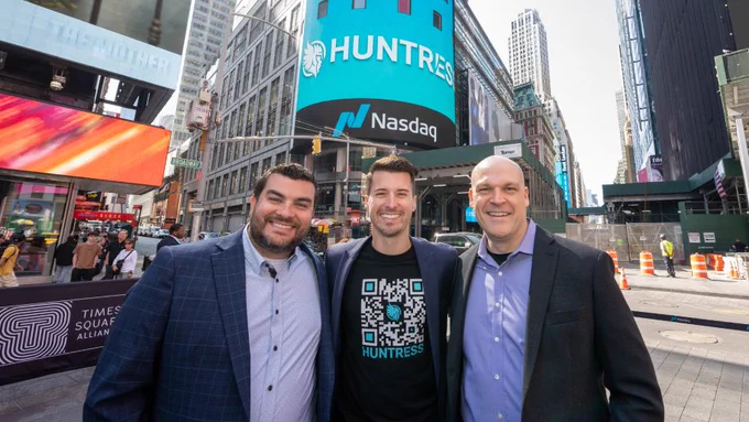 Three white men in blazers in front of Nasdaq Market