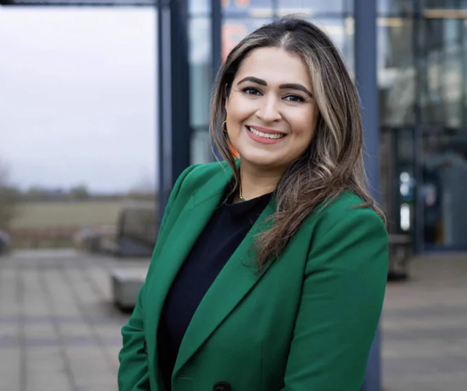 Umaima Ahmad stands side on to camera, smiling in an emerald green suit jacket and black top.