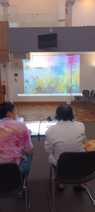 A participant with artist Georgia and a light box in a large room with their colourful swirling artwork projected onto the wall.