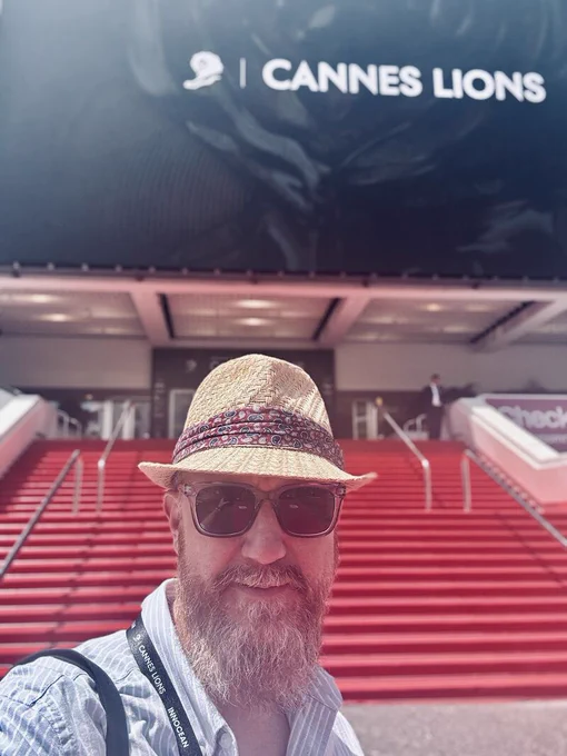 Tristan is in a hat and sunglasses in front of a Cannes Lions event venue: a big red staircase
