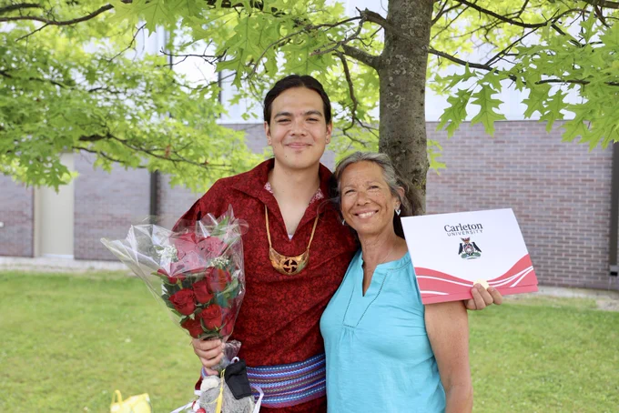 An indigenous student in traditional regalia smiles with their mother.