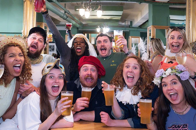A photo showing a group of performers holding beers in a bar
