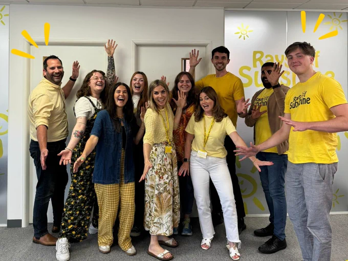 Group of office workers smile for the camera. They are all wearing some kind of yellow.