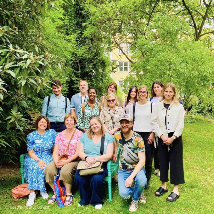 A group of decision makers in education from the UK on a visit to Berlin, outside in a park, some of them sitting on a turquoise bench. 