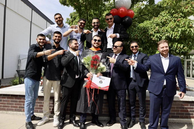A large group of friends and family celebrate their grad, pointing at him proudly.