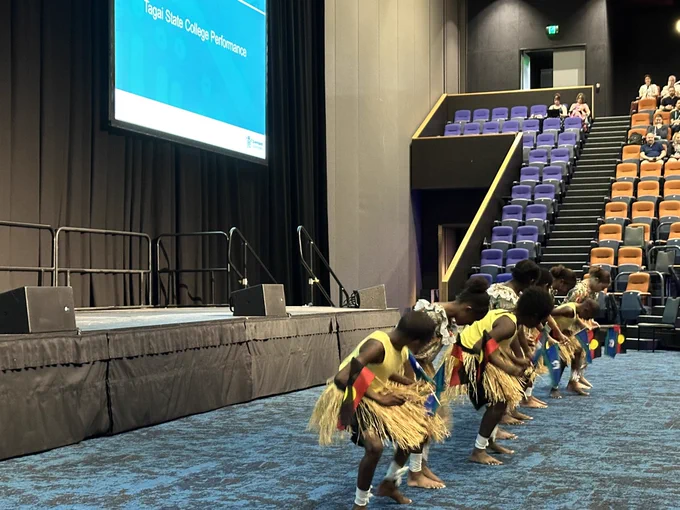 Elementary students wearing grass skirts performing a traditional dance on the auditorium floor.