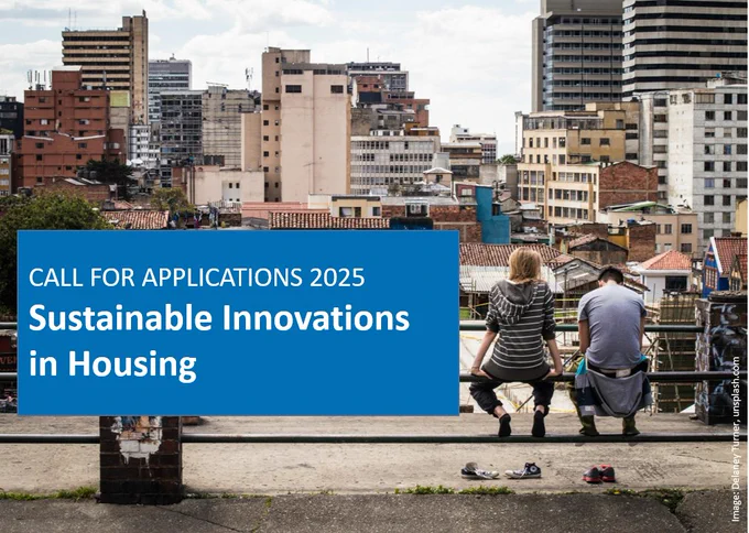 A man and a woman sit on a railing with their backs to the viewer, looking down on a city. In the foreground a banner: "Call for Applications 2025, Sustainable Innovations in Housing"