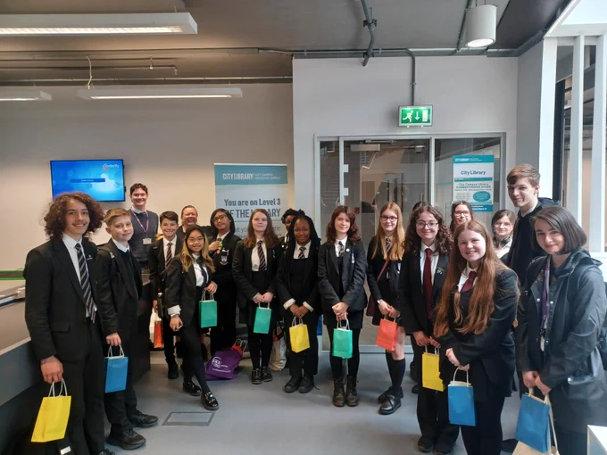Library assistants gathered around the City of Glasgow College Librarian and Library - all of the library assistants are holding colourful goody bags.