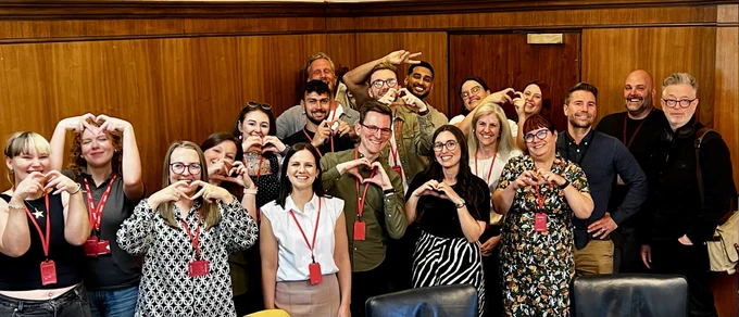 A group of people smiling at the camera making heart shapes with their hands 
