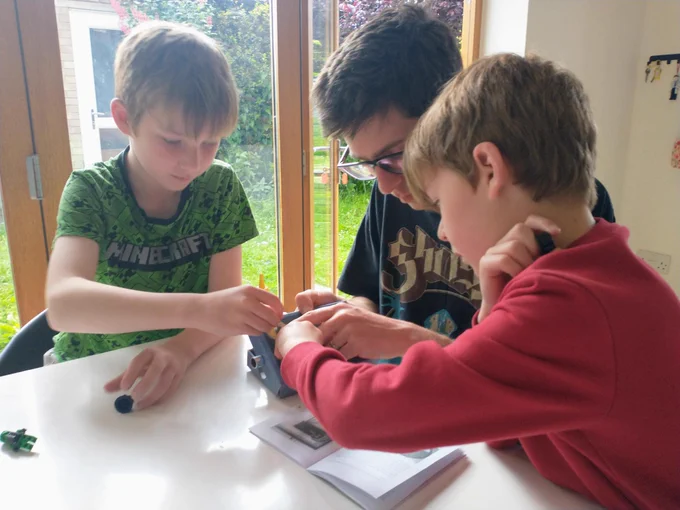 Two young boys side either side of their dad whilst helping to construct a bat detector on the table. 