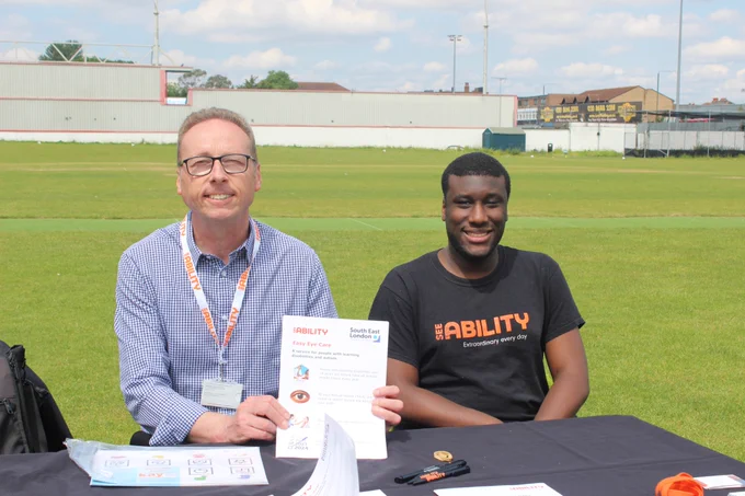 Steve and Lance at the SeeAbility stand with the sports field in the background. 