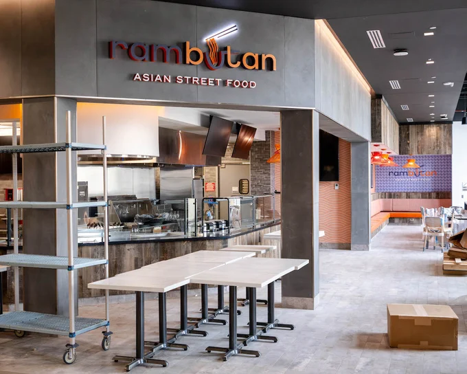 A dining venue with a purple and orange sign reading "rambutan." The walls surrounding are grey and purple. 