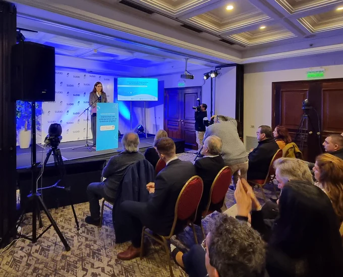 Ministra habla desde un escenario con una pantalla, frente al público. 