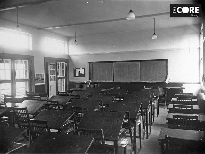 A black and white photograph of a 1930s classroom showing rows of school desks and chairs.