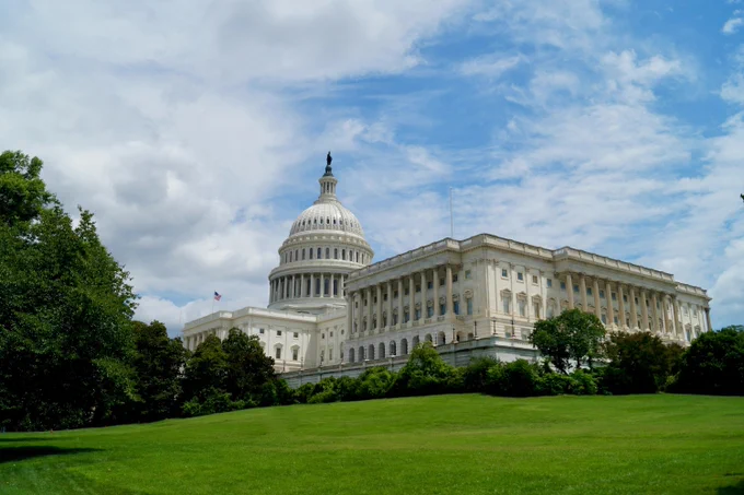 Exterior view of the United States Capitol Building with lush green lawns in the foreground.